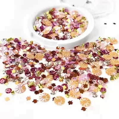 Confetes metálicos coloridos em formato de flores e círculos em superfície branca