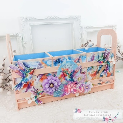 Organizador de madeira decorado com pássaros e flores coloridas, com texto inspirador e três divisórias azuis.