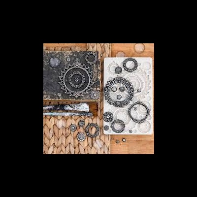 Conjunto de brincos e anéis de metal preto com detalhes florais sobre tábuas cinza e branca em tecido natural claro