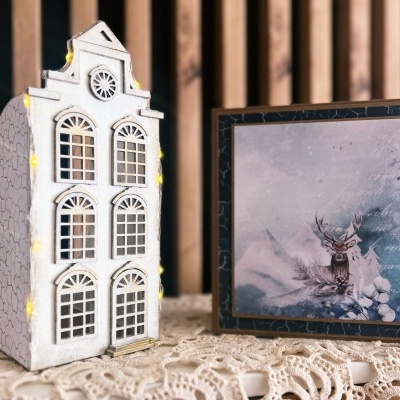 Casa decorativa branca iluminada e caixa quadrada com ilustração de veado em ambiente nevado