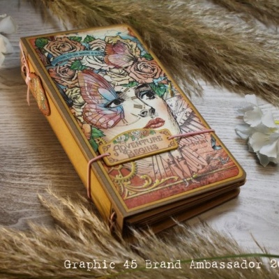 Caderno decorativo colorido com rosto feminino, flores e pássaro, texto A THOUSAND MEMORIES, elástico laranja, sobre madeira clara com flores e folhas