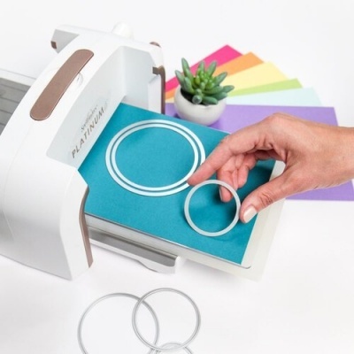 Máquina de corte de papel e círculos recortados em papel azul, fundo com planta e folhas coloridas