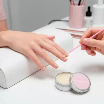 Pomada para cutículas Pro Cuticle Balm em lata de metal com tampa rosa aplicada numa unha em ambiente de manicure