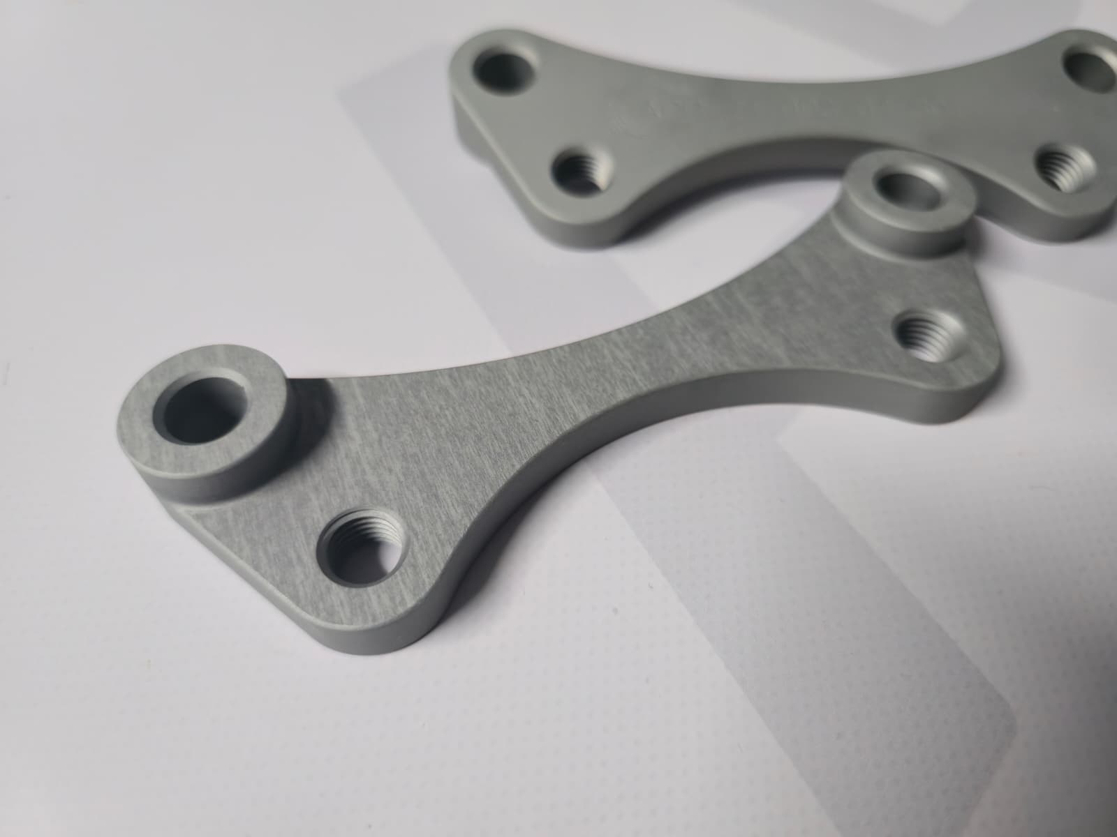 Two silver metal brackets with threaded holes on white surface