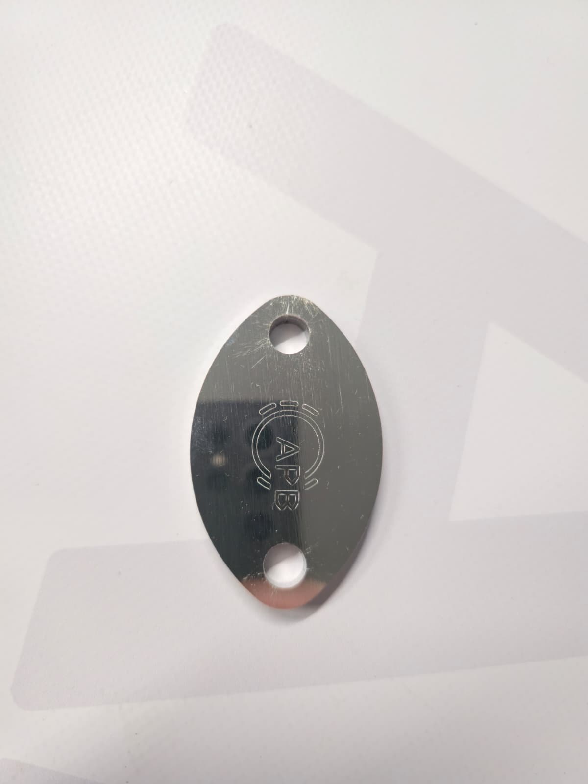 Oval metallic keychain with 'APE' engraving on a white surface