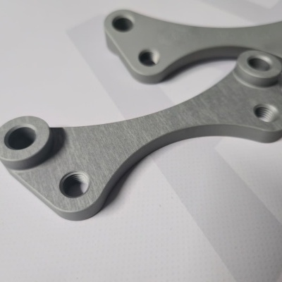 Two silver metal brackets with threaded holes on white surface