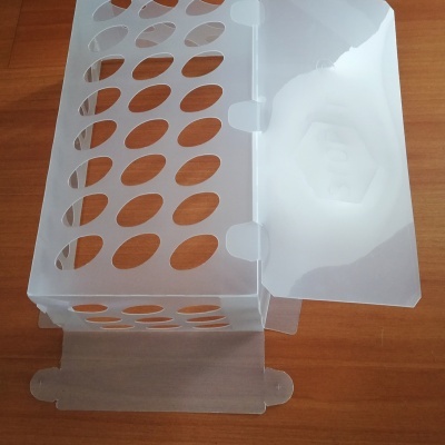 Caixa de plástico translúcido branco com orifícios ovais e tampa aberta sobre mesa de madeira