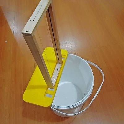 Espelho de madeira com base amarela sobre balde branco em chão castanho-laranja