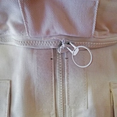 Casaco bege claro com fecho éclair e velcro, bolsos e costuras reforçadas.