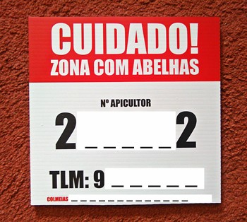 Placa de aviso em vermelho e branco com texto CUIDADO! ZONA COM ABELHAS e espaços para números
