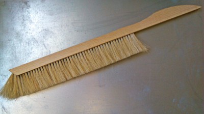 Vassoura fina de madeira com cerdas naturais sobre superfície metálica cinzenta