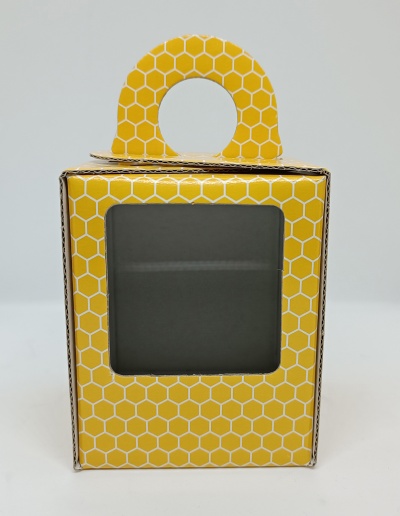 Caixa de papelão amarelo com padrão de colmeia, janela transparente e pega circular