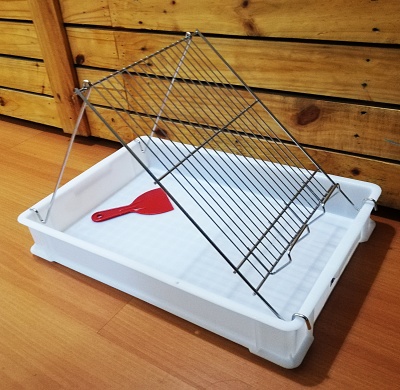 Suporte metálico com grelha inclinada numa bandeja de plástico branco com espátula vermelha