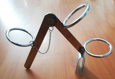 Suporte metálico prateado com três argolas grandes sobre superfície de madeira