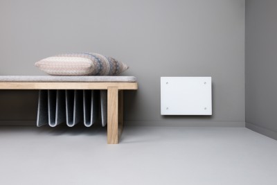 Banco de madeira clara com almofada e manta cinzenta junto a parede cinzenta com placa branca