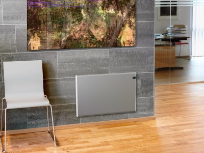 Radiador elétrico cinza claro numa parede de azulejos cinzentos ao lado de uma cadeira branca e pintura colorida