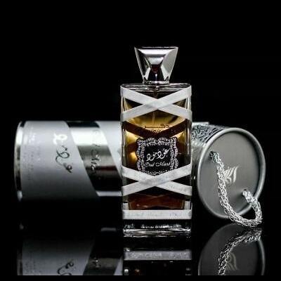 Frasco de perfume transparente com decoração em fita branca e embalagem cilíndrica prateada