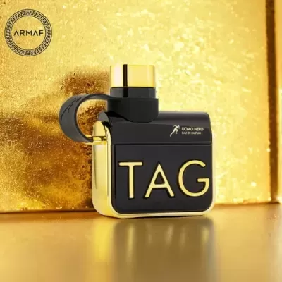Frasco de perfume preto e dourado com texto TAG em relevo dourado sobre fundo dourado
