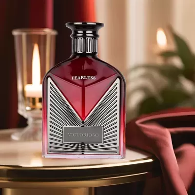 Frasco de perfume vermelho e preto com texturas geométricas numa mesa com vela acesa