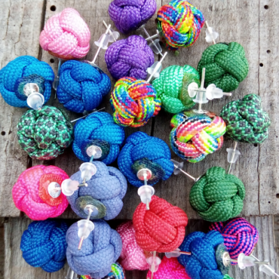 Brincos de nós de corda coloridos sobre madeira com etiqueta ART CORD