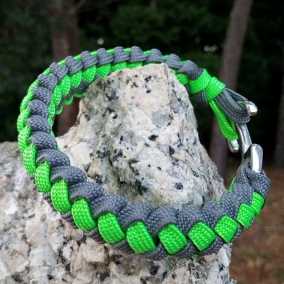 Pulseira trançada verde e cinzenta com fecho prateado sobre pedra