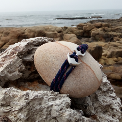 Pulseira azul com fecho prateado sobre pedra clara entre rochas à beira-mar