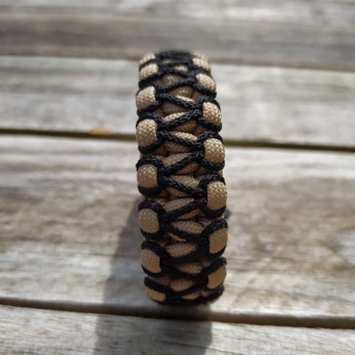 Pulseira trançada preta e bege sobre madeira clara