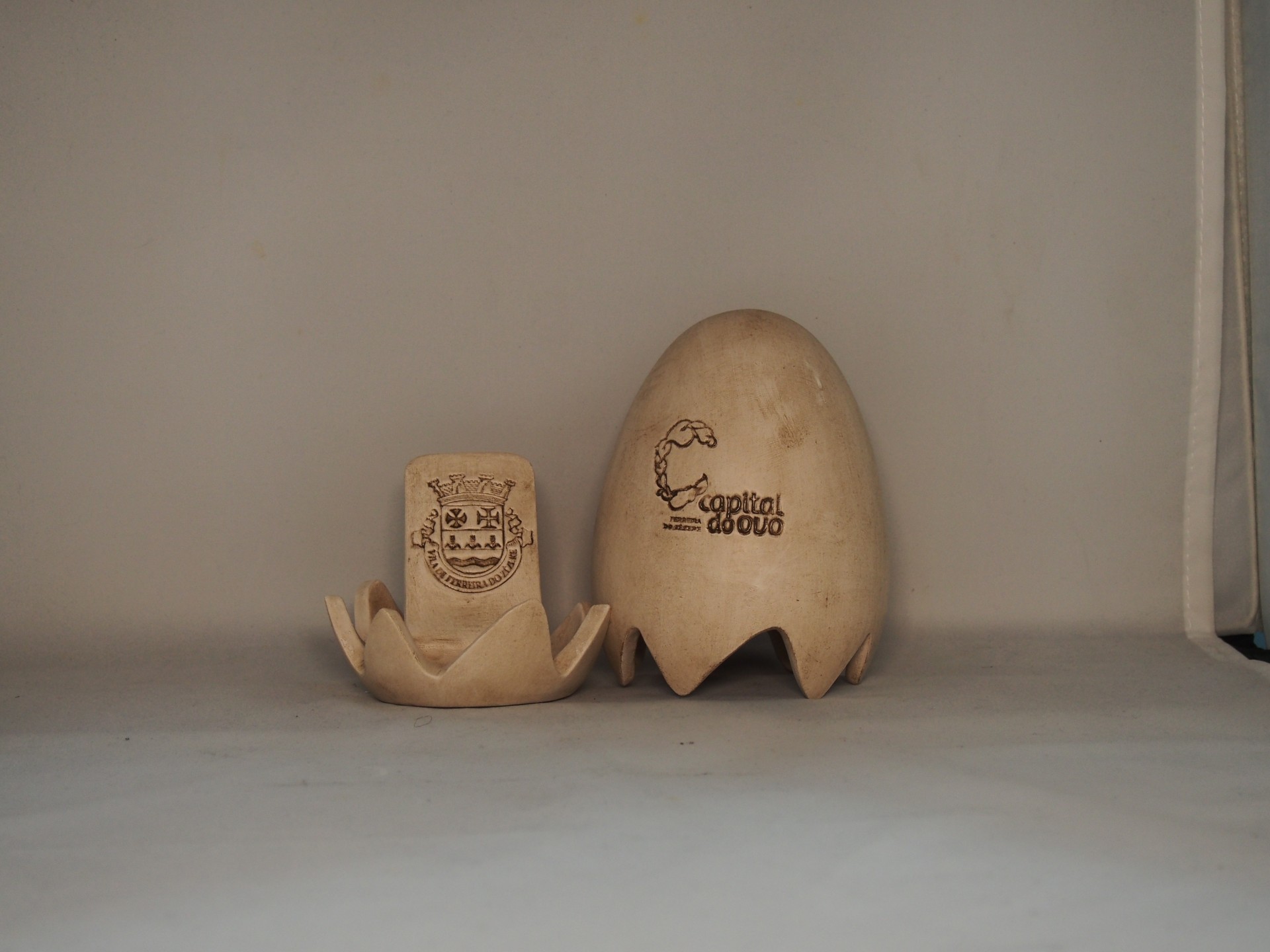 Dois objetos de cerâmica cor de areia, um com brasão e outro com texto Carnival Glow.