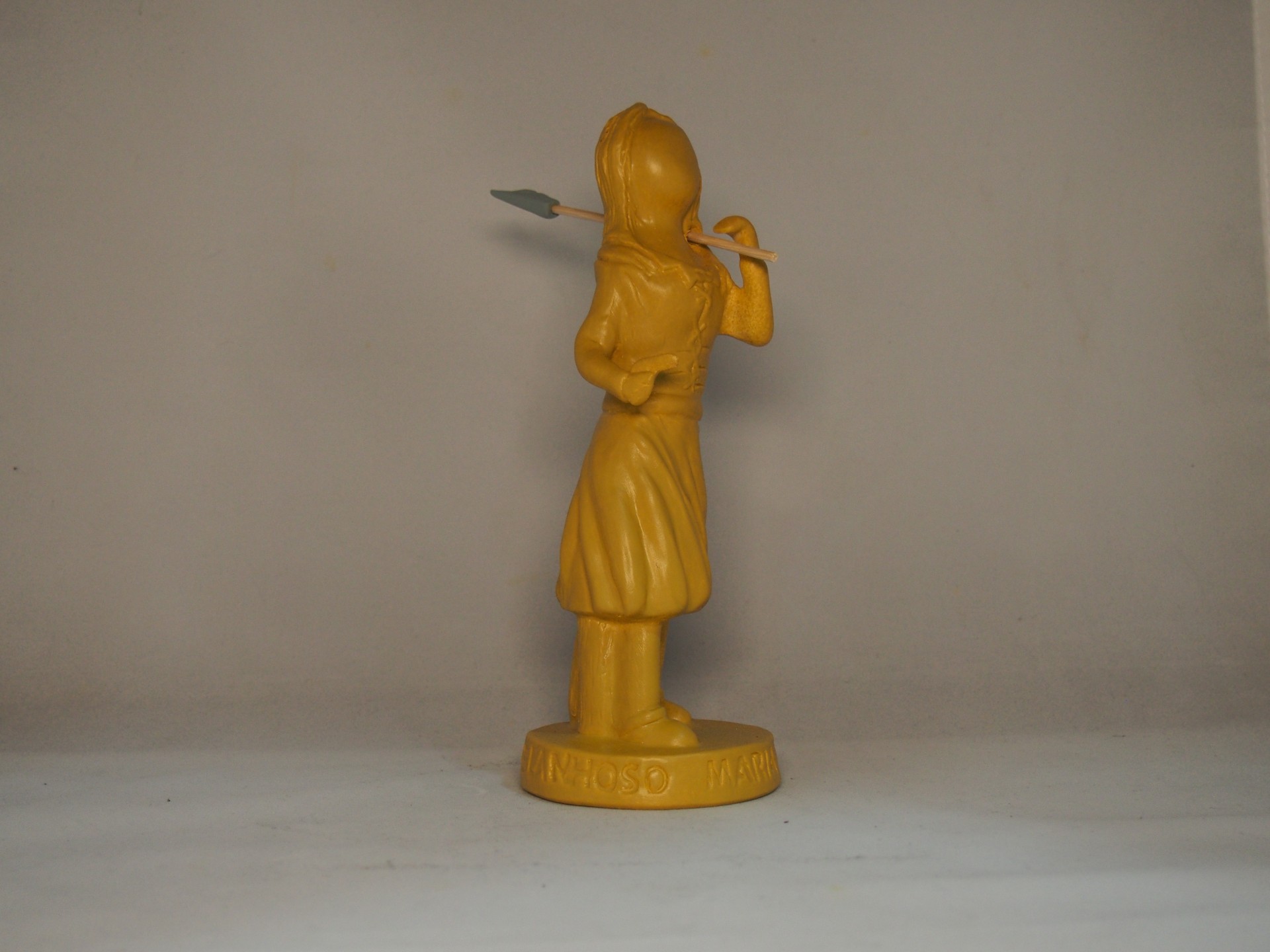 Estatueta amarela de figura feminina com lança sobre base redonda