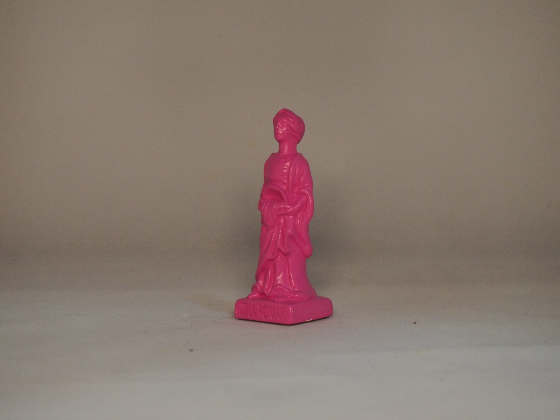 Pequena estátua cor de rosa de figura humana sobre superfície plana