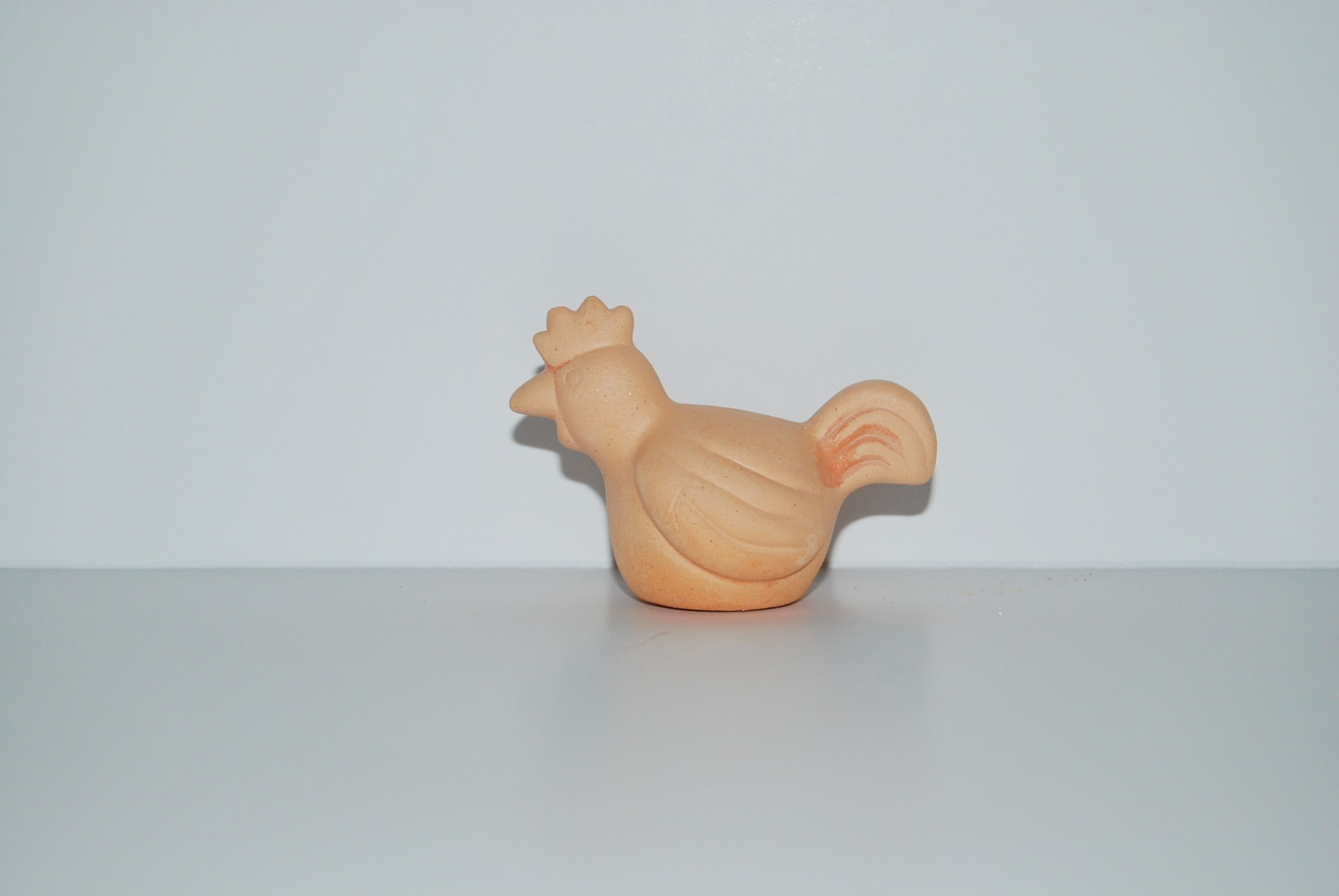 Figura em terracota forma de galinha sobre superfície branca