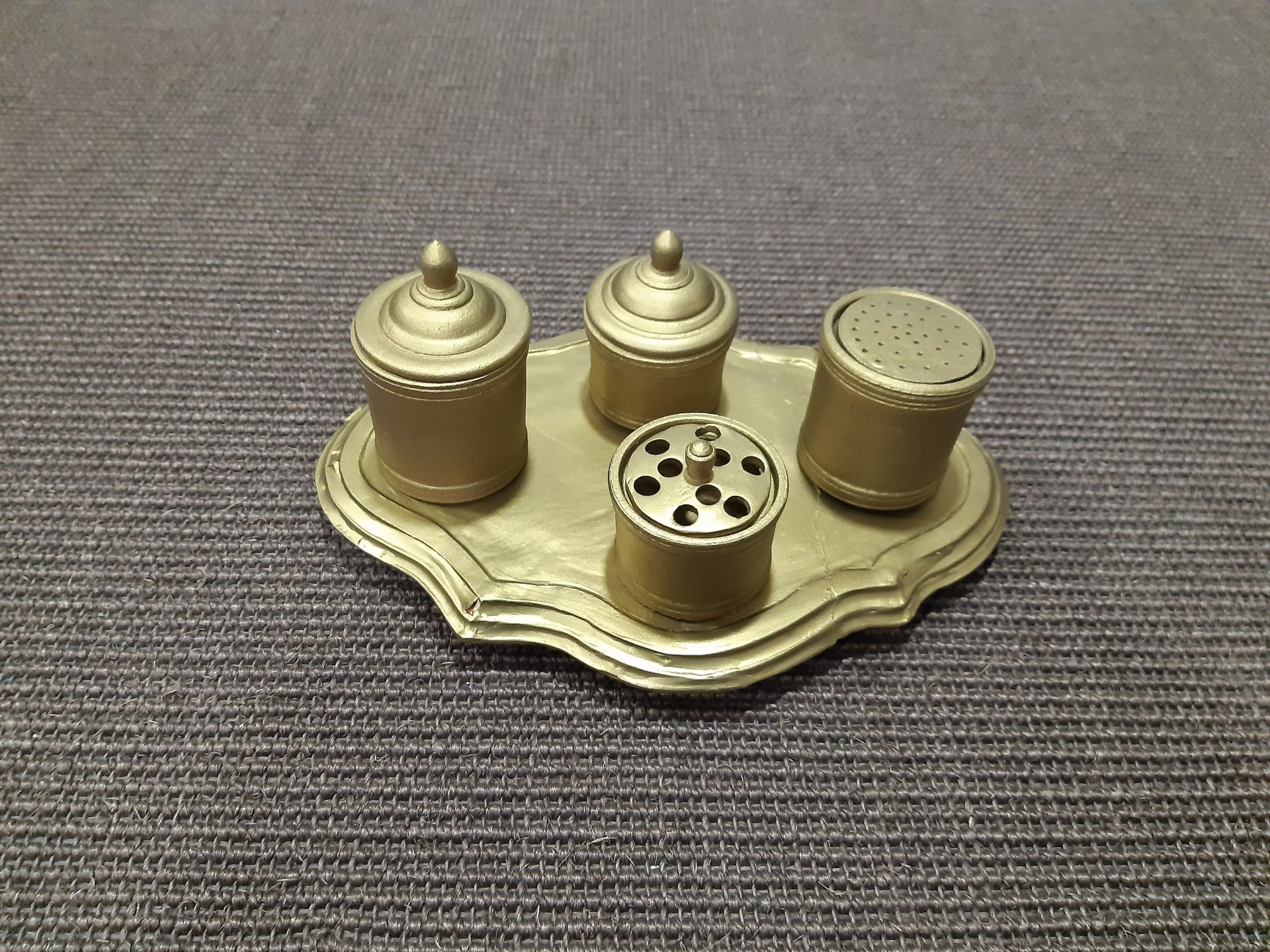 Conjunto de saleiro e pimenteiro dourado com base decorativa sobre tecido castanho.