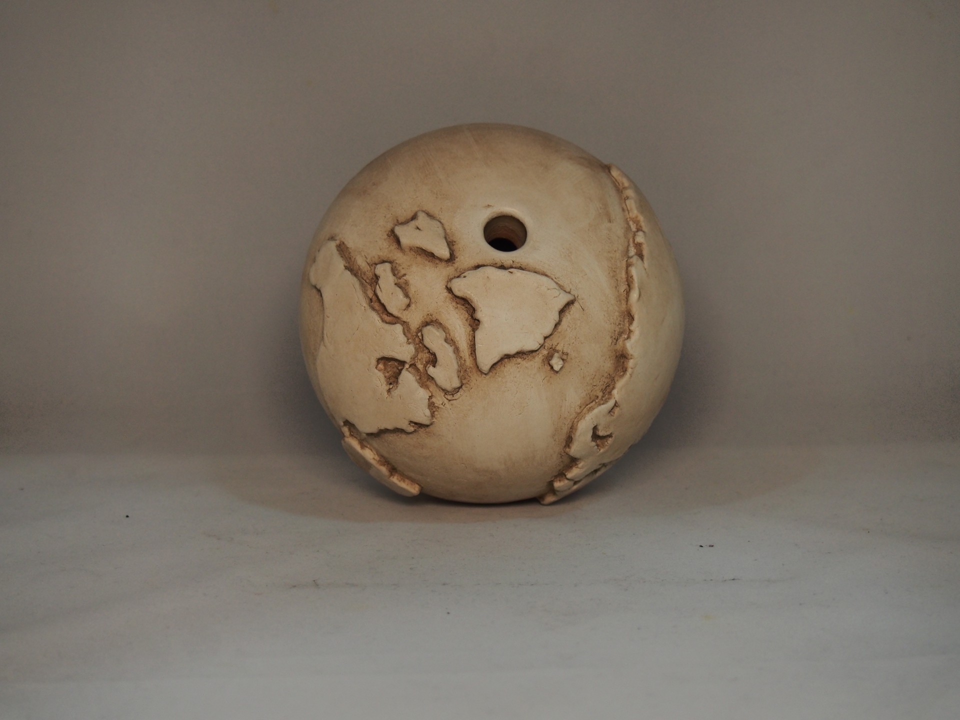 Bola de cerâmica bege com detalhes castanhos e buraco no centro em fundo cinza