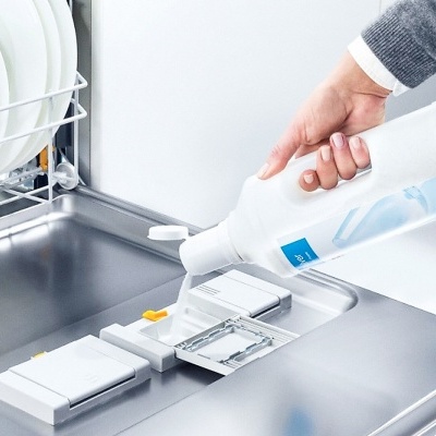 Mão a verter detergente em máquina de lavar loiça aberta com pratos brancos.