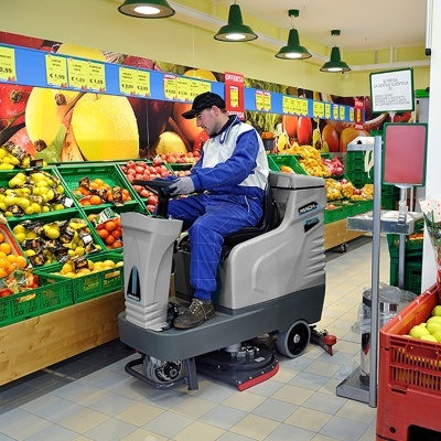 Homem a usar máquina de limpeza num supermercado junto a frutas e legumes.