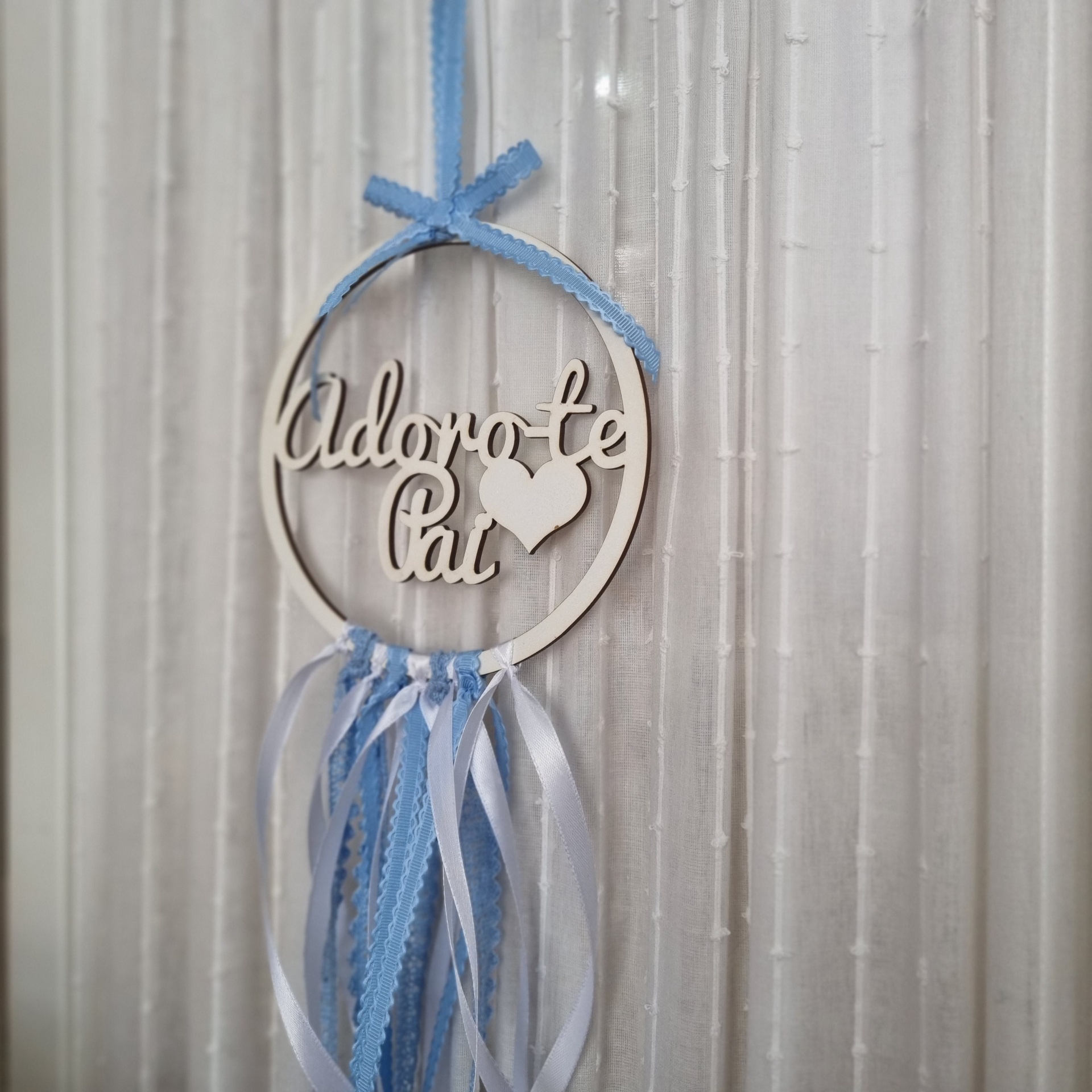 Enfeite pendurado com a frase Adoro-te Pai e fitas azuis e brancas