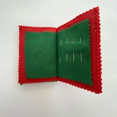 Estojo de agulhas vermelho com interior verde e agulhas inseridas