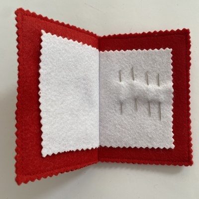Kit de costura pequeno com capa vermelha e interior branco com agulhas.