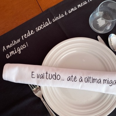 Conjunto de mesa com prato branco, talheres, guardanapo e pano de mesa com textos em português