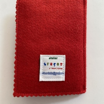 Estojo vermelho em feltro com etiqueta de tecido branca e texto colorido.
