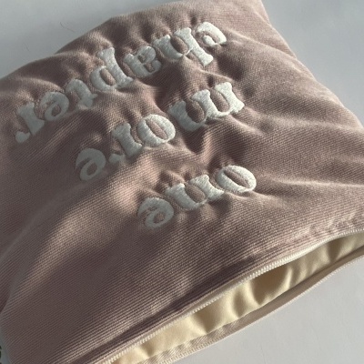 Bolsa rosa com bordado branco e texto invertido sobre fundo branco