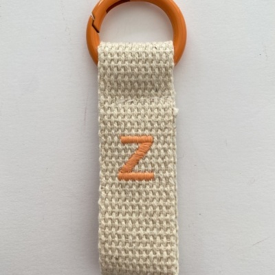 Chaveiro com argola laranja e tecido bege com letra Z bordada.