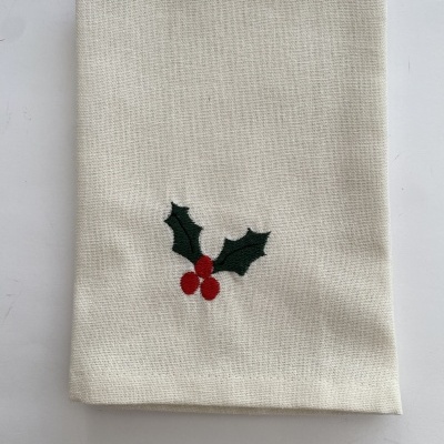 Guardanapo de tecido cru com bordado de folhas de azevinho verdes e bagos vermelhos.