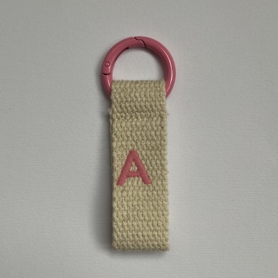 Porta-chaves com argola rosa e tira de tecido bege com letra A rosa