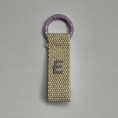 Porta-chaves com argola roxa e tira de tecido bege com letra E bordada