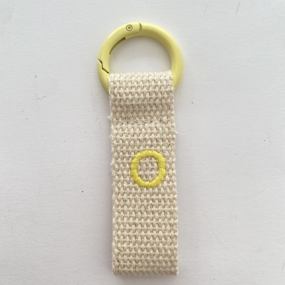 Porta-chaves com argola amarela e fita bege com círculo amarelo bordado