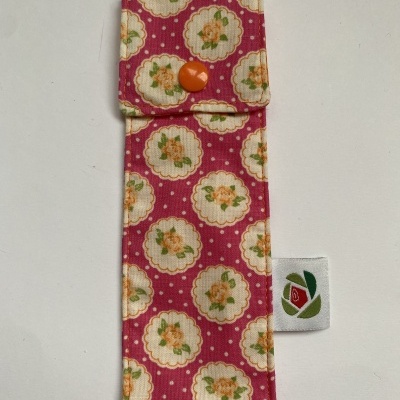 Estojo de tecido floral rosa com botão laranja e etiqueta branca
