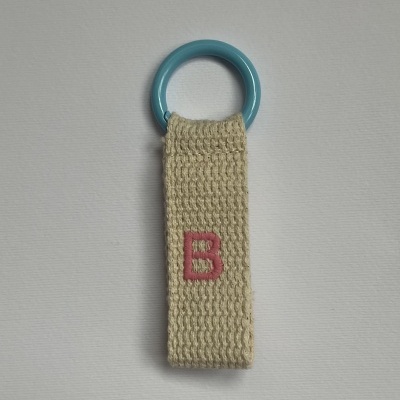 Argola azul com fita de tecido bege e letra B rosa