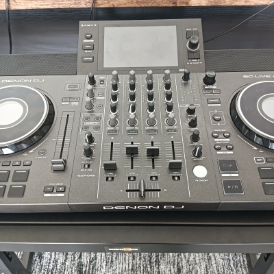 Controladora DJ Denon DJ preta com ecrã e botões numa mesa preta e madeira.