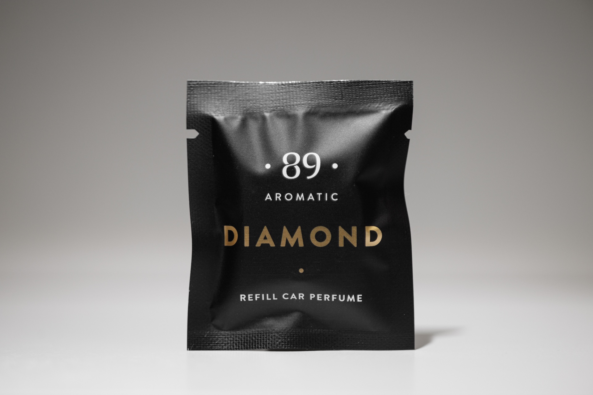 Pacote preto de plástico fosco com texto branco e dourado, perfume para carro